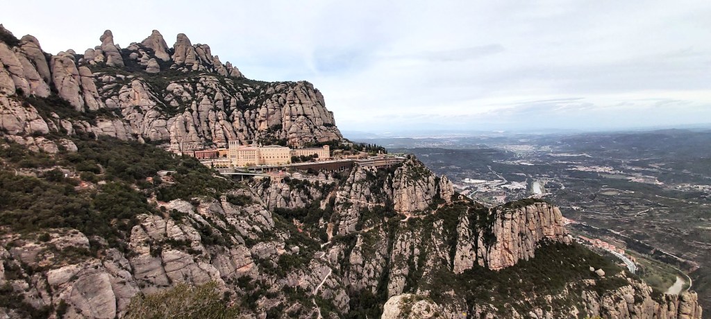 Scenic view of Montserrat mountains with the iconic Montserrat Cathedral nestled among rocky peaks under a clear blue sky in Catalunya, Spain