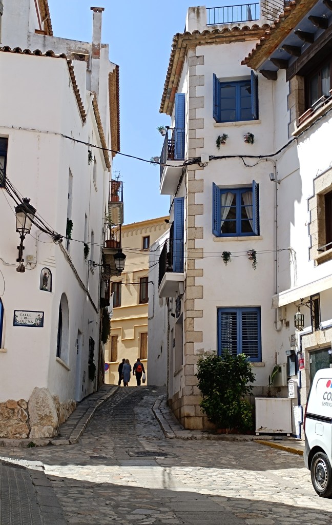 Charming narrow street in Sitges Old Town lined with whitewashed buildings and colorful shutters.