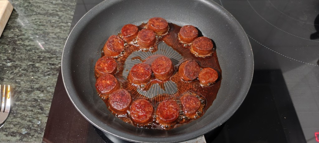 Chorizo slices added to the pan, beginning to sizzle and release their oils.