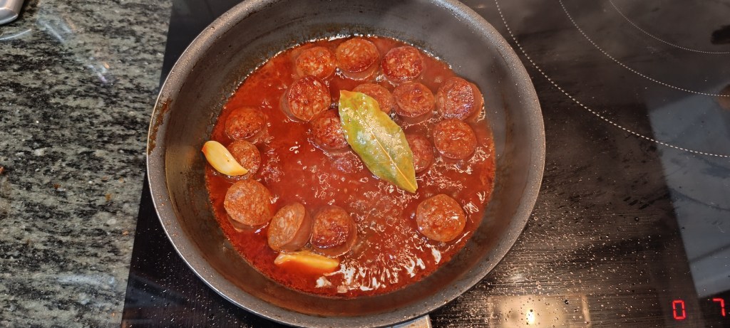  White wine being poured into the pan with sizzling chorizo and garlic, creating a fragrant simmer.