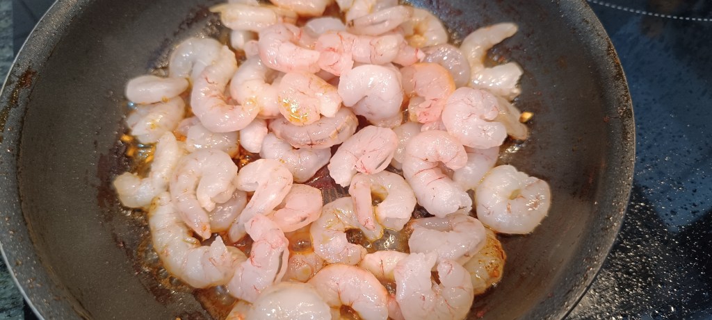 Raw prawns added to the pan, turning pink as they cook in the bubbling garlic and chili oil.
