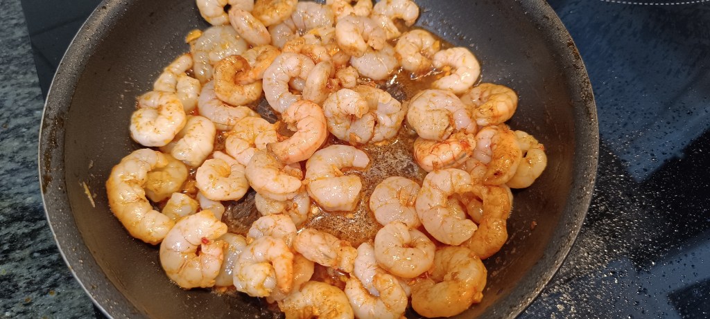 Raw prawns added to the pan, turning pink as they cook in the bubbling garlic and chili oil.