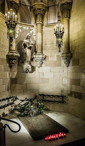 Antoni Gaudí’s grave in the crypt of the Sagrada Família, Barcelona, marked by a simple stone tomb surrounded by candles and floral tributes