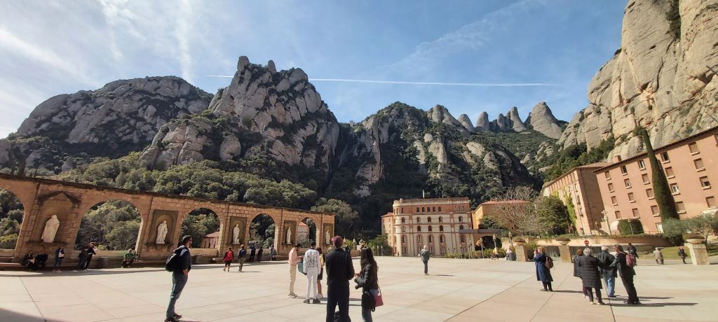 Panoramic view of Montserratโs rugged peaks with the famous Montserrat Cathedral at the base, showcasing the unique blend of nature and architecture in Catalunya