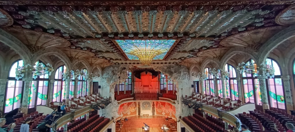 Interior of the Palau de la Música Catalana featuring a stunning stained-glass skylight, ornate balconies, and elaborate decorative details