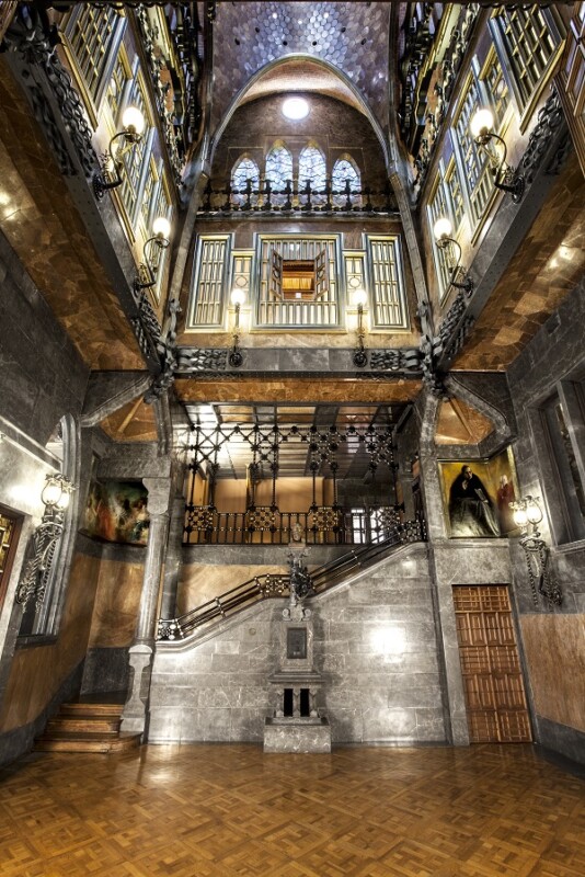Lavish interior of Palau Güell featuring intricate woodwork, decorative ceilings, and elegant design by Gaudí.
