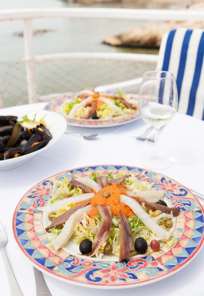 Colorful Sitges-style salad with mixed greens, tuna, anchovies, and boiled egg on a white ceramic plate