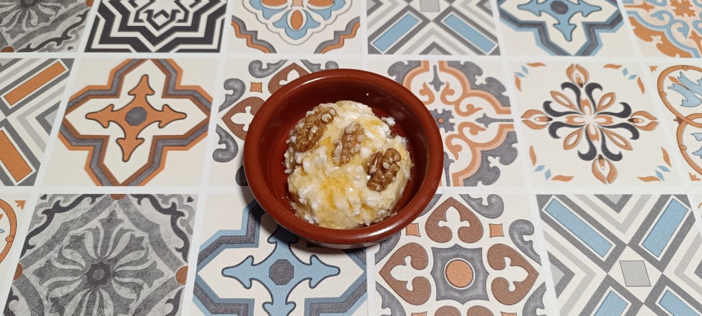 Close-up of mató amb mel, a traditional Catalan dessert featuring creamy fresh cheese topped with golden honey and crunchy walnuts, served on a decorative ceramic tapas plate over vibrant Spanish tiles.