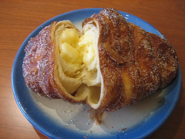 A golden, flaky pastry filled with creamy custard, lightly dusted with sugar, served on a small plate.