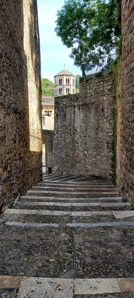 Narrow stone alleyway in Girona’s old town, flanked by historic buildings with textured walls and small windows.