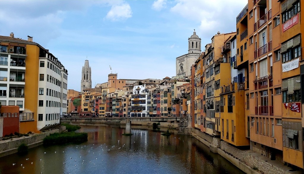 View of the colorful riverside buildings along the Onyar River in Girona, Spain, with the Girona Cathedral and bell tower in the background