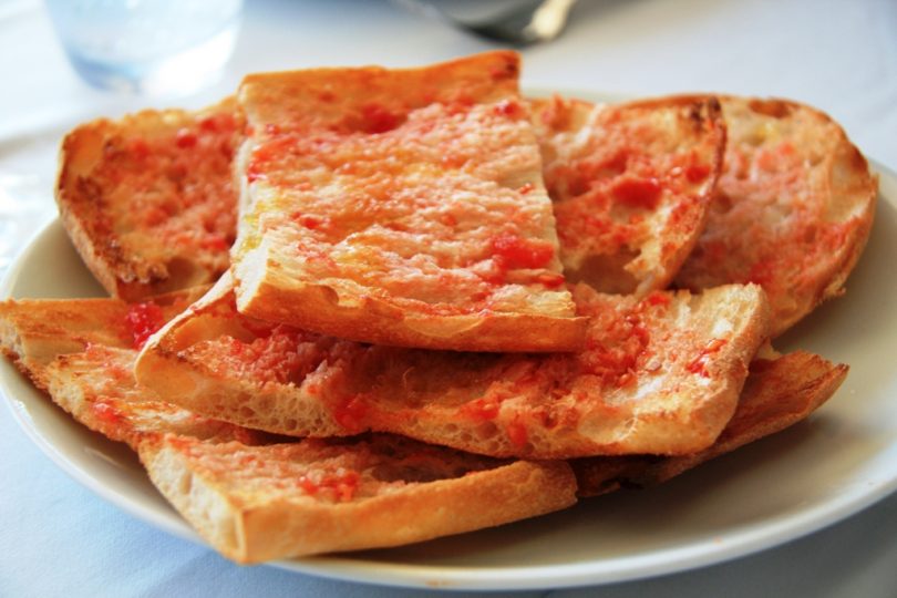 A slice of toasted bread rubbed with ripe tomato, drizzled with olive oil, sprinkled with salt, and served on a rustic plate.
