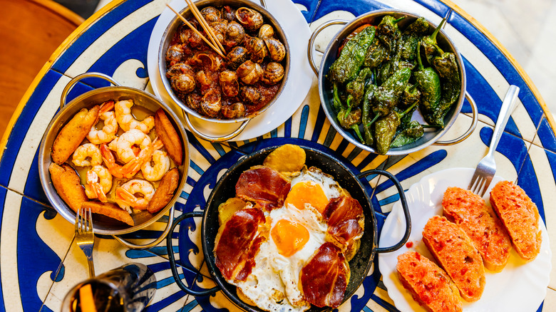 Assorted Spanish tapas including croquetas, gambas al ajillo, jamón ibérico, and pintxos on a colorful table