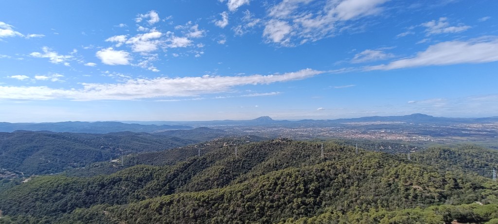 Expansive view from Tibidabo overlooking Barcelona, blending city rooftops with the blue horizon of the sea, Andorra, and Montserrat on a cleara day.