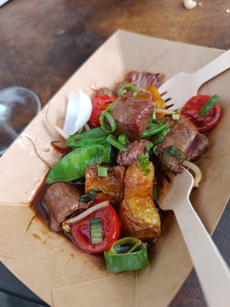 Crowd gathered around grills watching chefs cook over live fire.