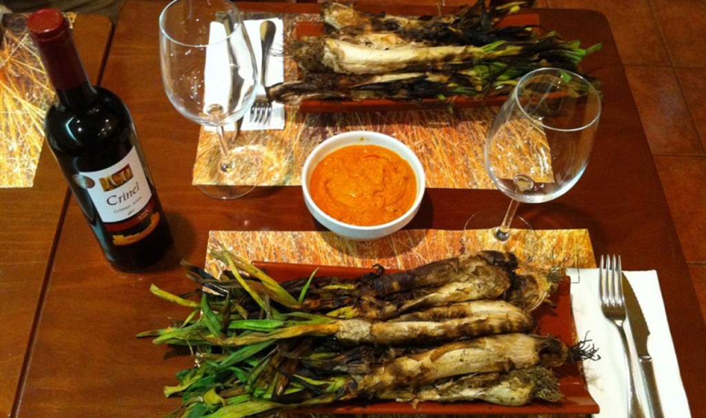 Grilled calçots served on a tray, blackened from the fire and ready to be dipped in romesco sauce.