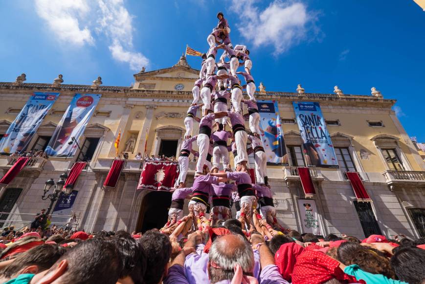 A team of castellers forming a human tower in a city square, watched by a gathered crowd.