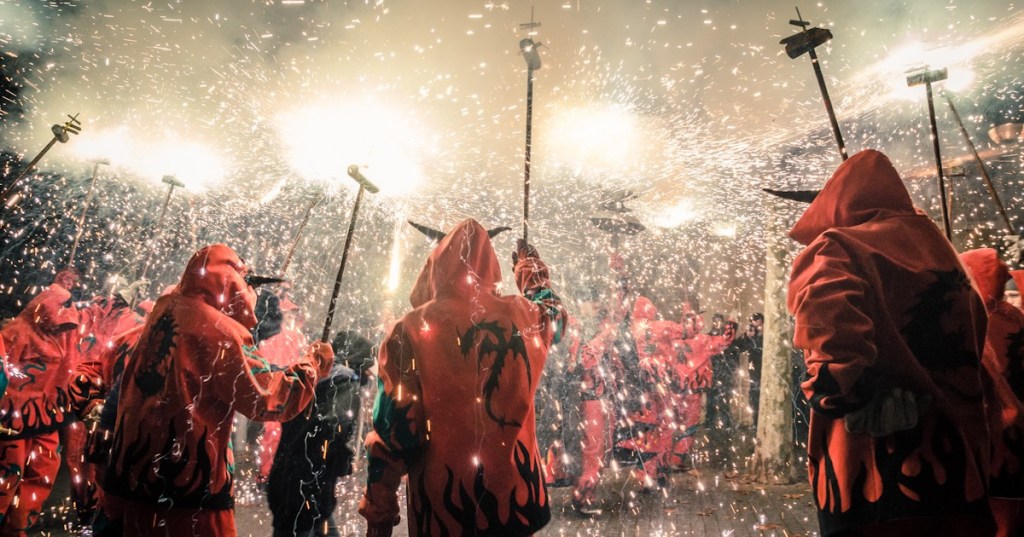 Performers dressed as devils running through the street surrounded by sparks and fireworks during a correfoc.