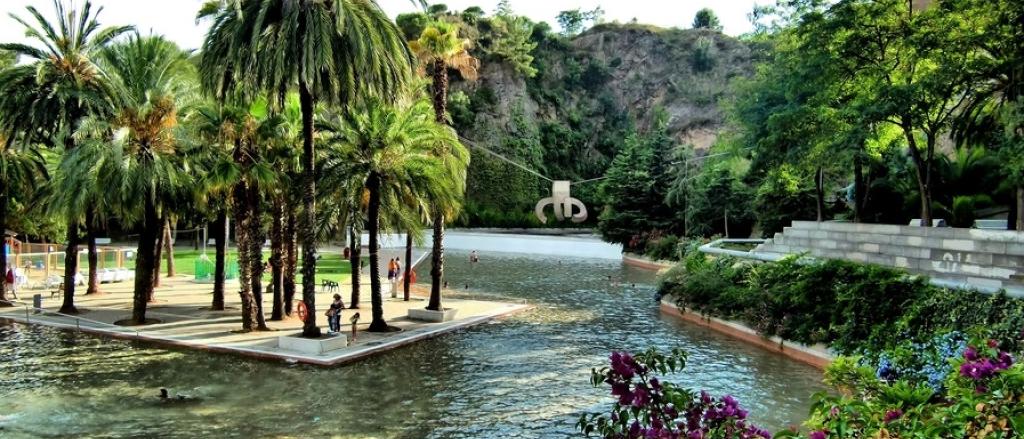 Parc de la Creueta del Coll in Barcelona during the day, with a reflecting pool, stone quarry walls, and the suspended Chillida sculpture.