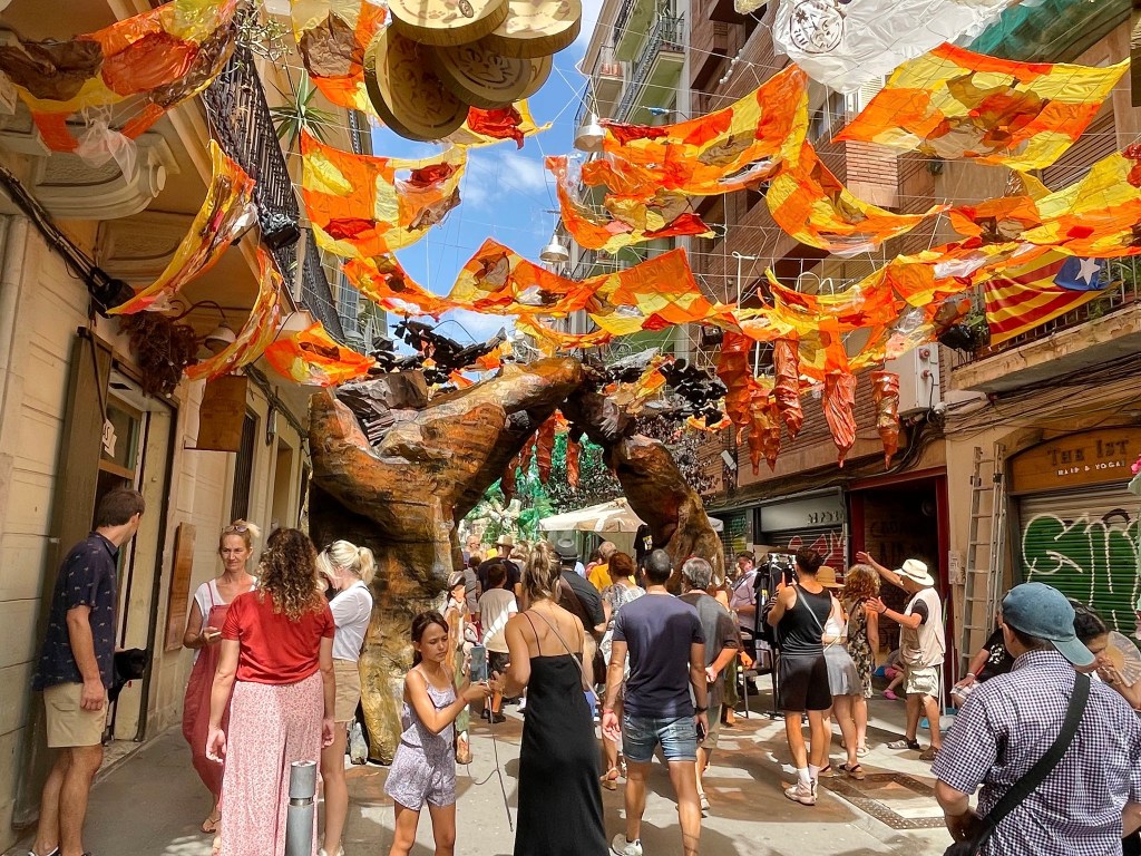 Narrow neighborhood street covered in colorful themed decorations during a festa major.