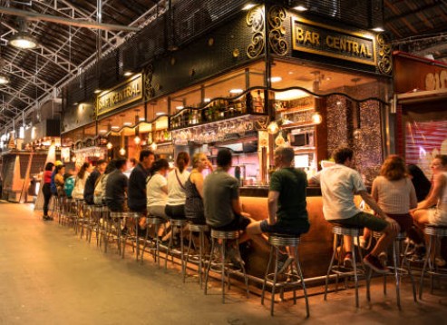 Friends laughing and chatting at a market bar in Barcelona, drinks on the table