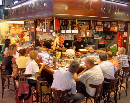 People sitting around a small bar inside a Barcelona market, enjoying drinks and tapas
